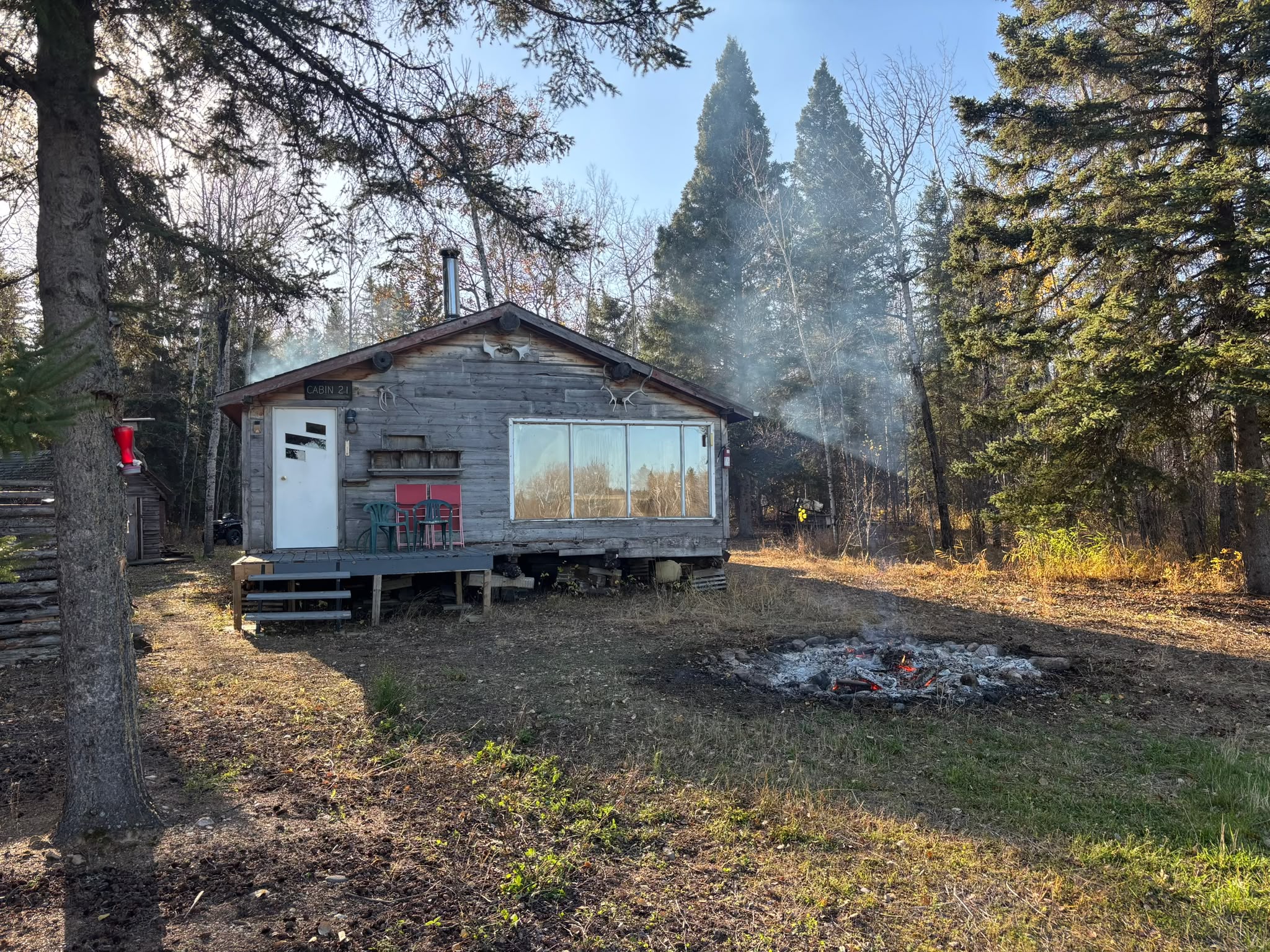 Rustic cabin with smoke from chimney and fire pit in foreground